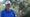 jay don blake waves toward a camera in a blue shirt and white hat